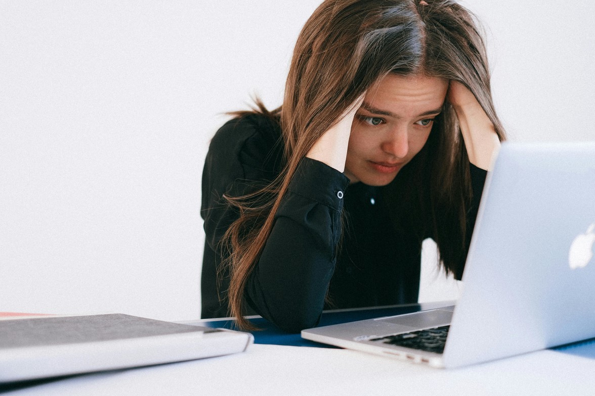 Woman with brown hair sitting thinking at desk, hands in her hair looking concerned