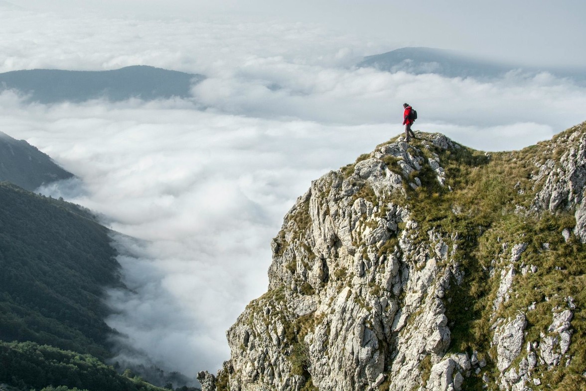 Man standing at peak of mountain in all his gear, beautiful sky in background and clouds